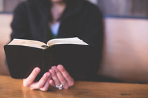 Hands holding a Bible on a wood table.