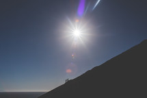a sunburst and men hiking up a steep mountain 