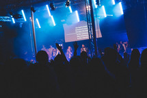 lyrics on a projection screen and worship leaders performing on stage 