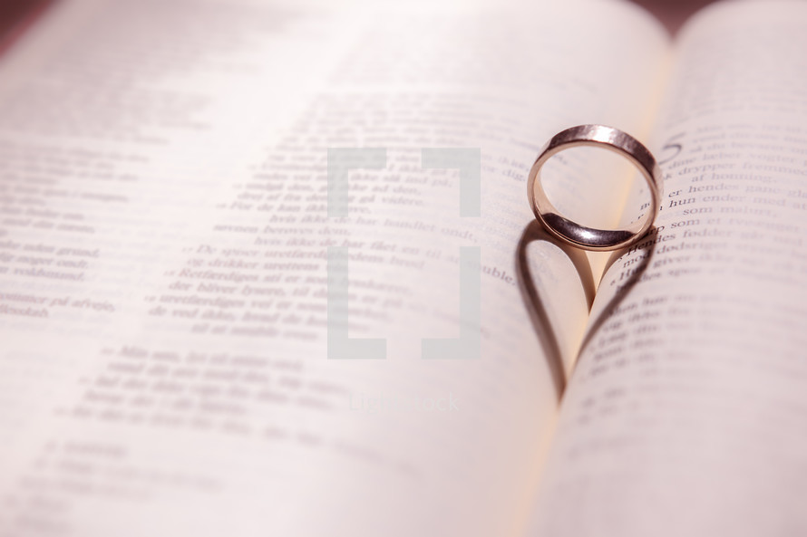 a wedding band forming a shadow in the shape of a heart between the pages of a Bible 