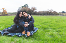 happy couple snuggling on a blanket in the grass