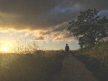 a boy child walking down a path in the distance at sunset 