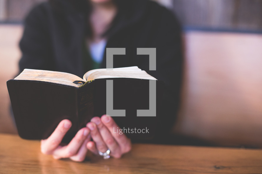 Hands holding a Bible on a wood table.