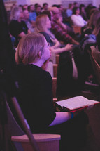 a woman with her hand over her mouth and Bible in her lap during a worship service 