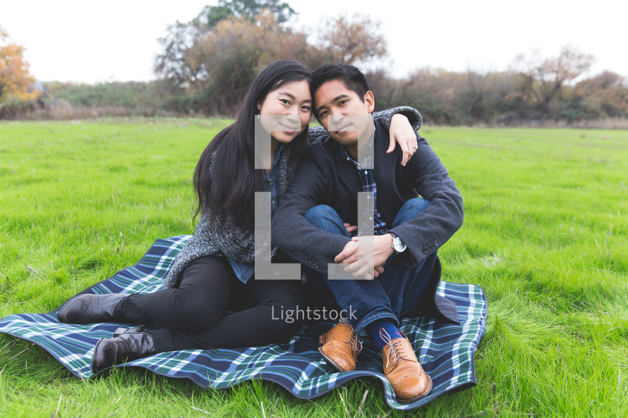 happy couple snuggling sitting on a blanket in the grass