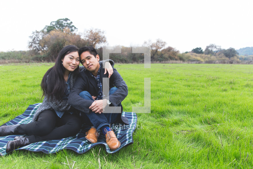 happy couple snuggling sitting on a blanket in the grass