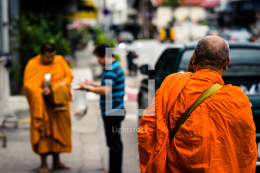 Buddhist monks in orange robes walking on a sidewalk 