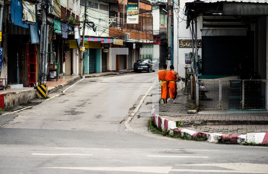 Buddhist monks in orange robes walking down a sidewalk 