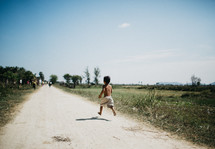 a boy child running down a dirt road 