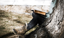 a woman in boots reading a Bible under a tree 