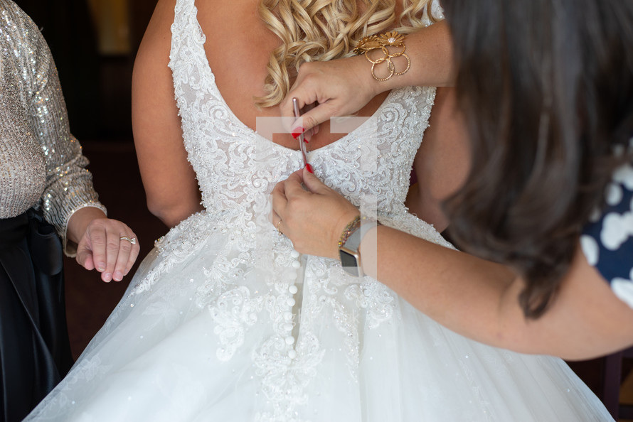 Women buttoning bride's wedding dress