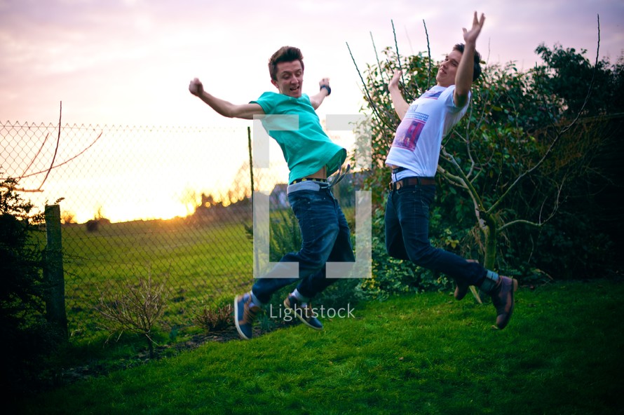Two boys jumping in the grass at sunset.