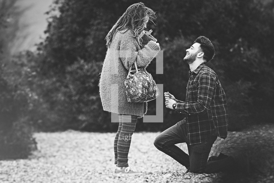 A young man on one knee proposing to a young woman.