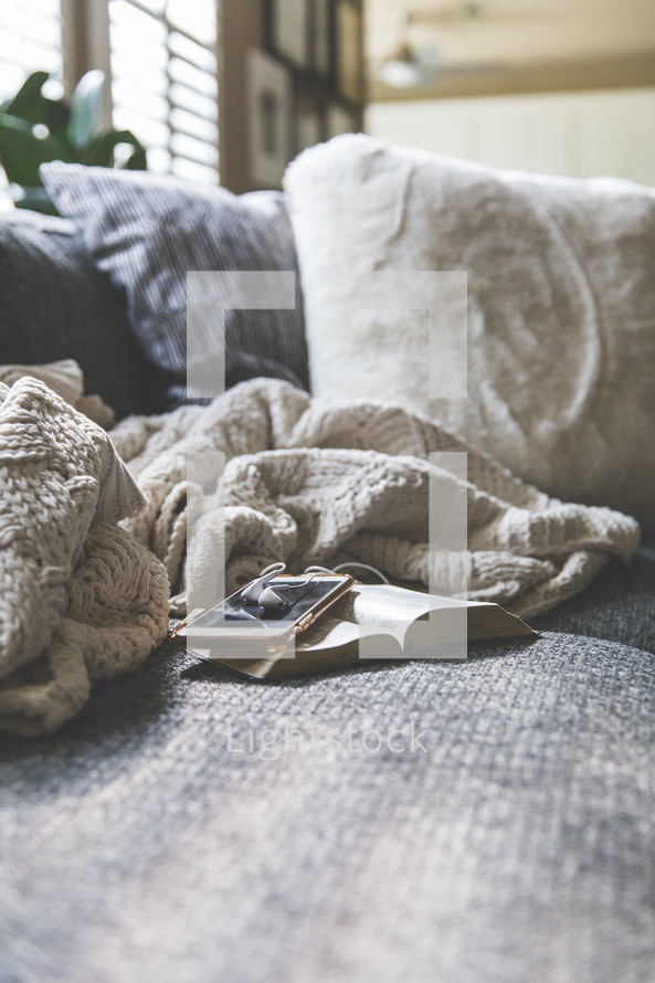 blanket, cellphone, earbuds, and open Bible on a couch 