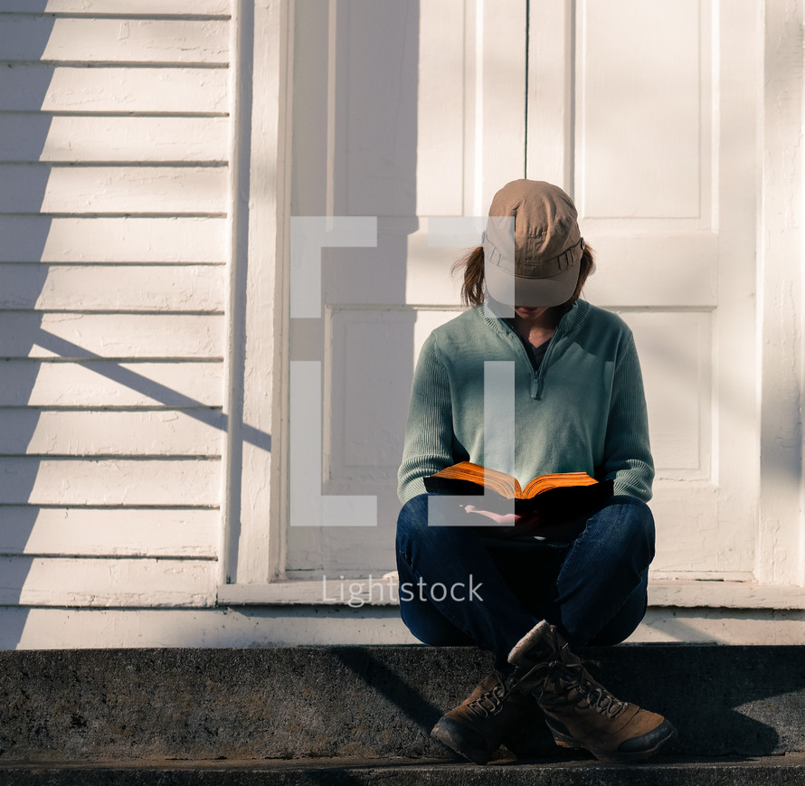 a woman in boots sitting on steps in front of a church holding a Bible 