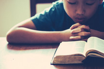child praying in front of a Bible 
