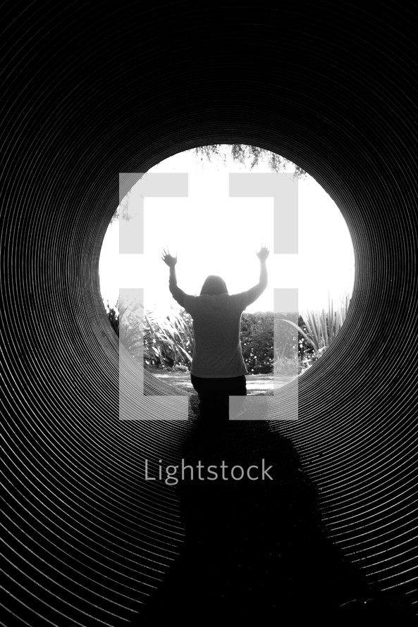 woman with her arms raised in worship sitting in a tunnel 