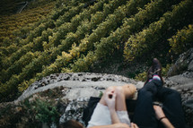 woman dangling her feet off the side of a cliff over a vineyard