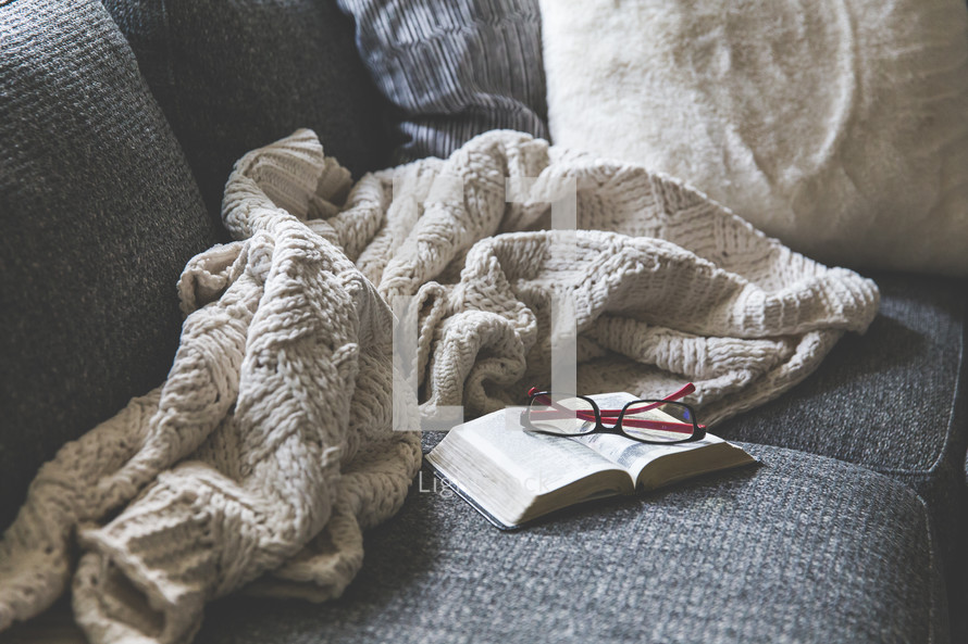 blanket, reading glasses, and open Bible on a couch 