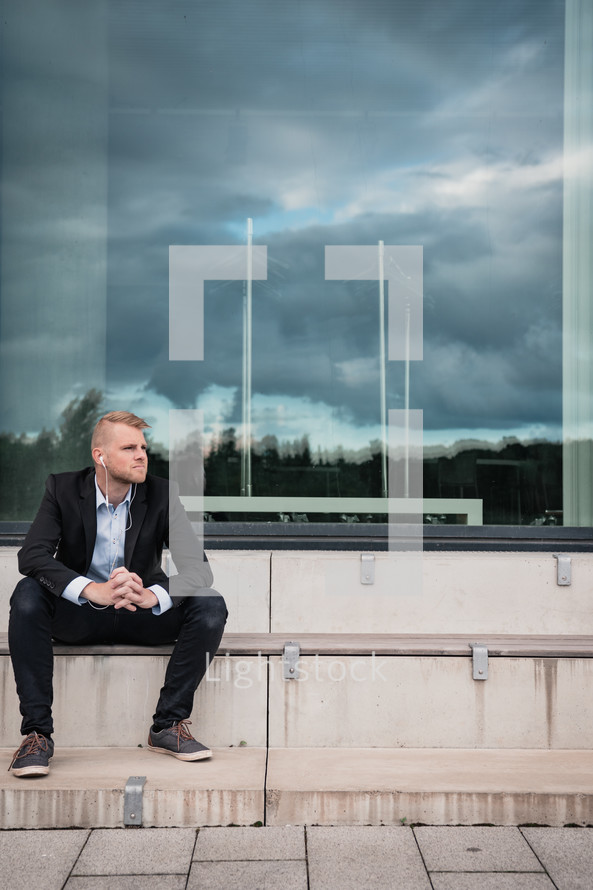 a business man sitting on steps with a reflection of a stormy sky in a window 