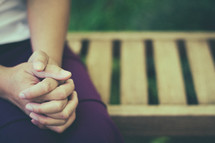 woman with praying hands sitting on a bench 