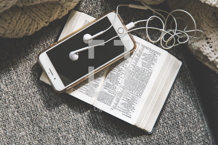 blanket, cellphone, earbuds, and open Bible on a couch 
