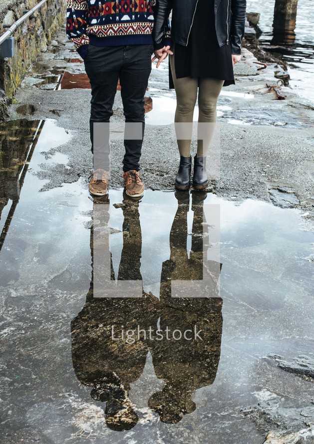 a couple standing near a puddle holding hands 