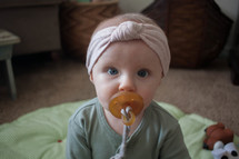 a baby girl with a pacifier in her mouth sitting on the floor on a blanket 