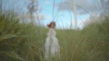 a woman in a long dress walking through a field of tall grasses 