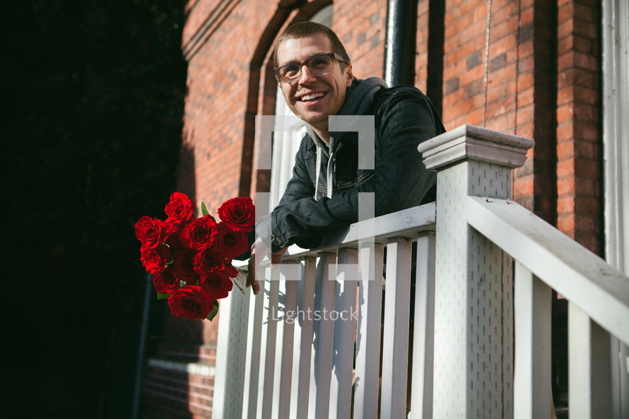A man standing over a railing holding red roses. 