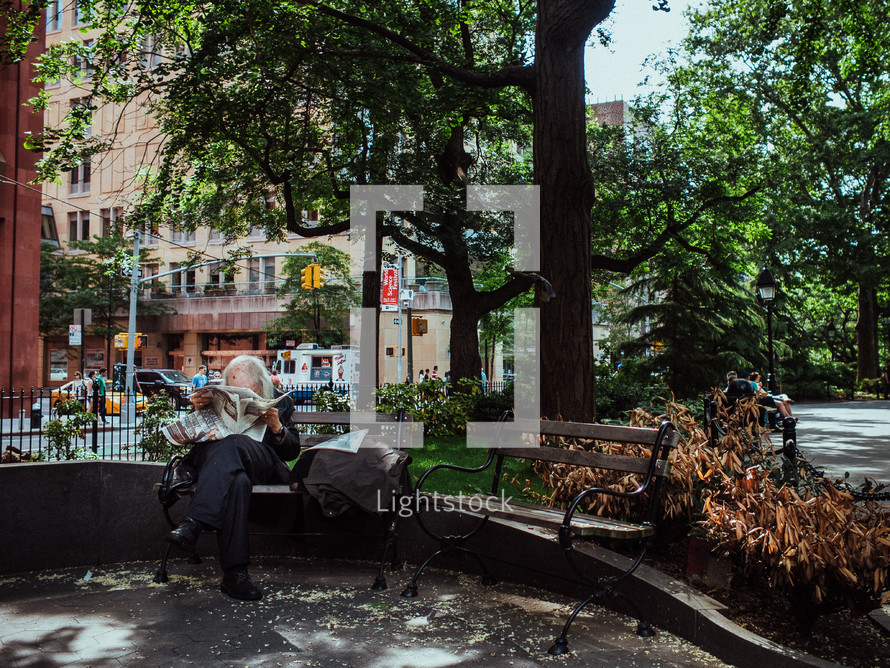 man reading a newspaper on a park bench 