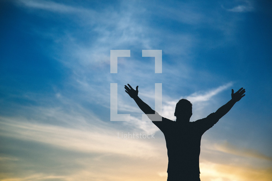 A silhouette of a man standing with hands raised in worship to God 