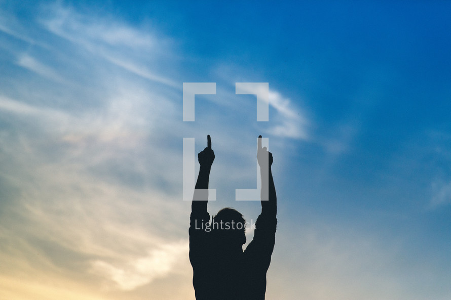 Silhouette of a man with arms raised pointing to the sky.