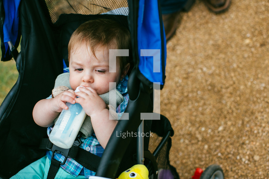 Infant drinking from a bottle while riding in a stroller.