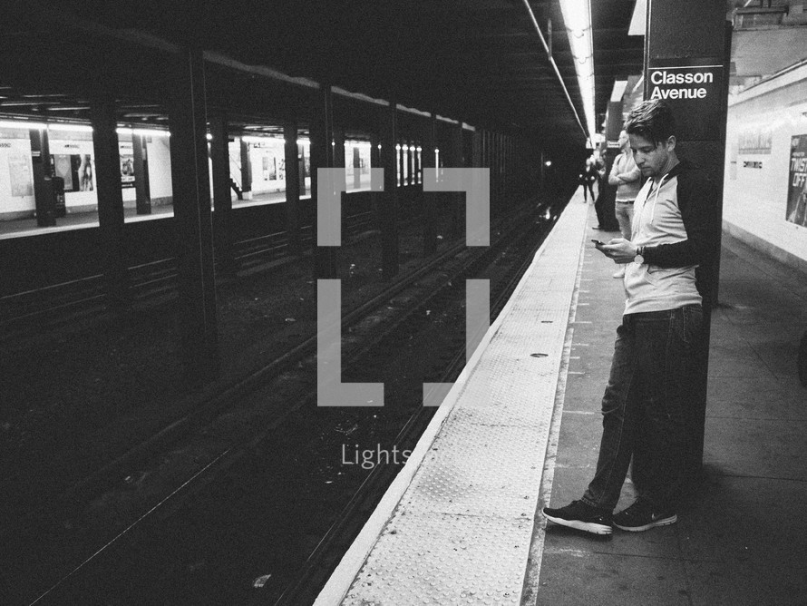 man checking his phone waiting for a subway train 
