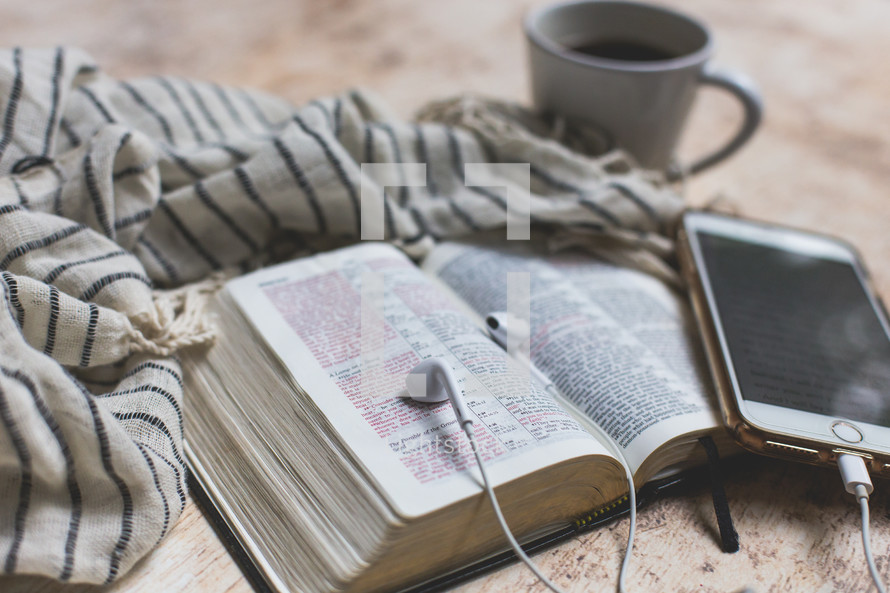 open Bible with coffee mug, cellphone, earbuds, and scarf 
