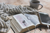 open Bible with coffee mug, cellphone, earbuds, and scarf 