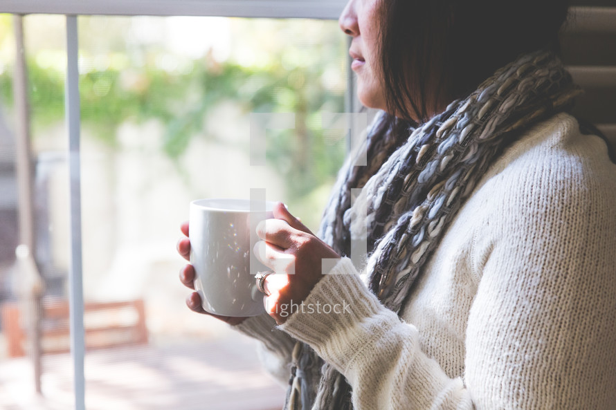 a woman looking out a window holding a coffee cup 