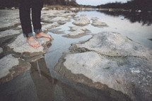 man's bare feet standing on rocks near a river 