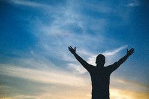 A silhouette of a man standing with hands raised in worship to God 