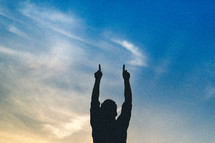 Silhouette of a man with arms raised pointing to the sky.