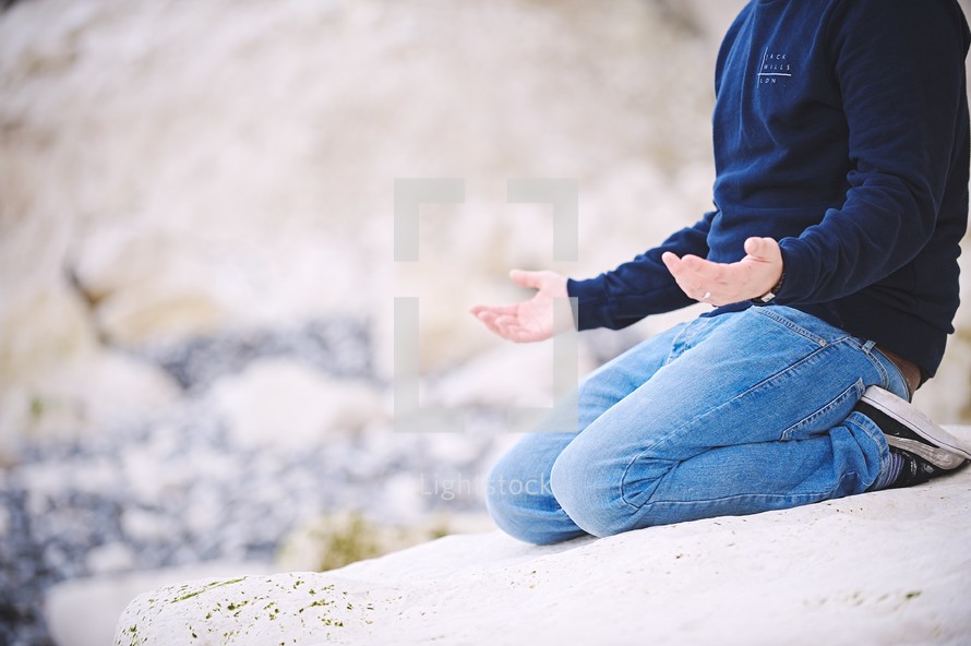 a man kneeling in prayer on a rocky shore 