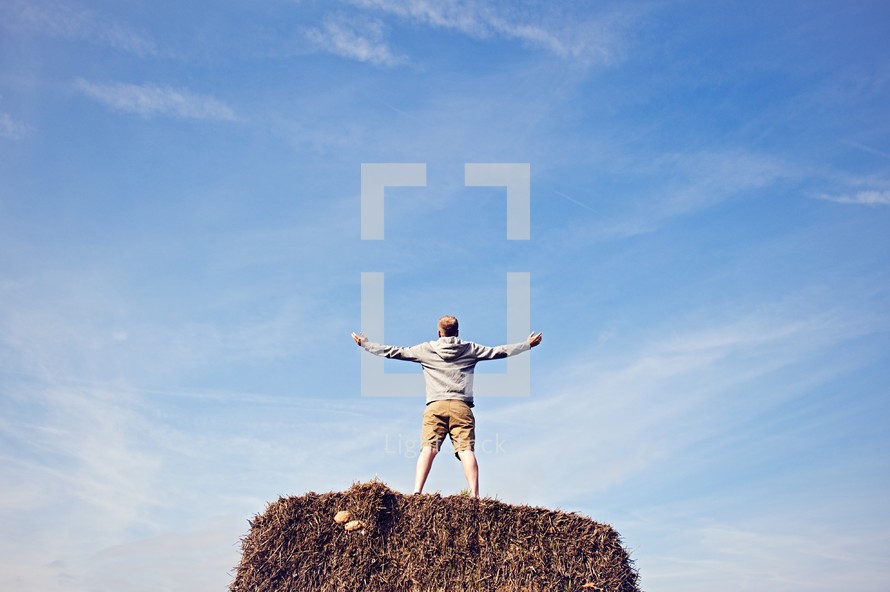 a man with outstretched arms standing on a hay bale 