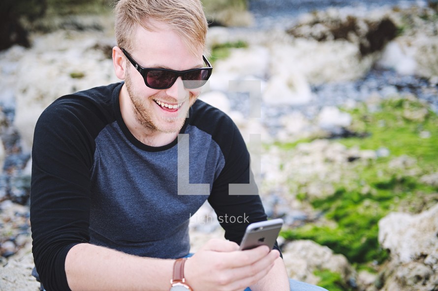 a man sitting on a rock texting on a cellphone 
