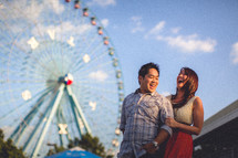 A couple laughing in front of a ferris wheel at the fair