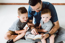 a Christian father reading a Bible to his sons 