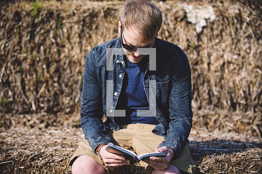 a man reading a Bible sitting on a hay bale 