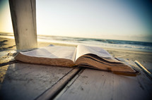 Open Bible on a wooden deck on the beach at the ocean.