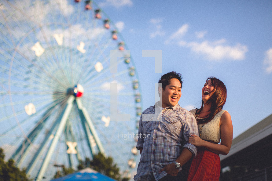 A couple laughing in front of a ferris wheel at the fair
