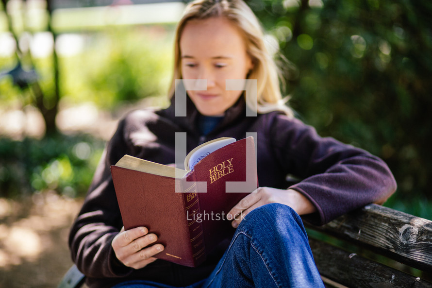 woman sitting on a park bench reading a Bible